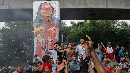 Protesters celebrate beside a defaced portrait of Prime Minister Sheikh Hasina after news of her resignation, in Dhaka, Bangladesh. (AP)