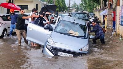 People try to move a vehicle stuck in a pit on a waterlogged road amid torrential rains in Jammu. (ANI) People try to move a vehicle stuck in a pit on a waterlogged road amid torrential rains in Jammu. (ANI)