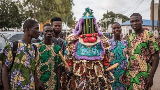 Visitor pose with an egungun, a character wearing a Yoruba costume and mask, during the grand procession of traditional masks in Porto-Novo. The Porto-Novo Mask Festival, which was held over three days, was created at the initiative of the Beninese government and the municipality, to replace the Porto-Novo International Festival usually held in January. During this new event, dozens of people wearing different masks from all over the country paraded, but also others from Togo and Burkina Faso were also exhibited on the main avenue of the city. (Photo by Yanick Folly / AFP)