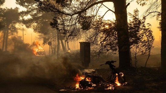 A motorbike and a car burn along a road during a wildfire in Varnavas, north of Athens, on August 11, 2024. (AFP)