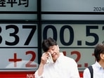 A passerby gestures in front of an electronic board displaying the Nikkei stock average outside a brokerage in Tokyo, Japan. 