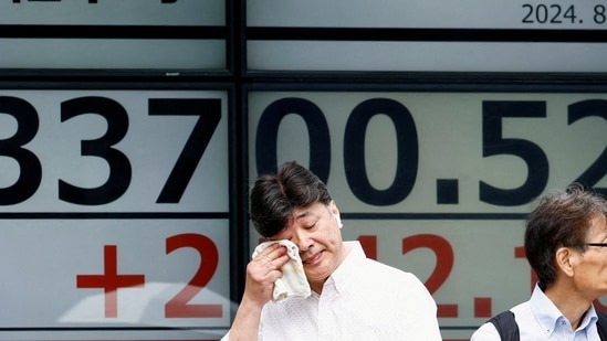 A passerby gestures in front of an electronic board displaying the Nikkei stock average outside a brokerage in Tokyo, Japan. (Reuters)