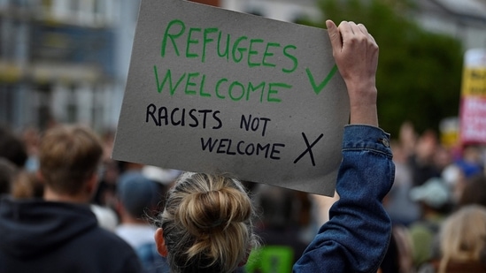 A protester holds a placard during a counter demonstration against an anti-immigration protest called by far-right activists, outside the Asylum Welcome immigration support service offices in Oxford, western England on August 7, 2024. (Photo by JUSTIN TALLIS / AFP)