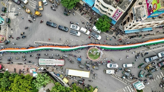 An aerial view shows school students carrying a large Indian national flag on a road during the 'Har Ghar Tiranga' campaign on the eve of the country's Independence Day celebrations in Vijayawada on August 14, 2024. (Photo by Idrees MOHAMMED / AFP)