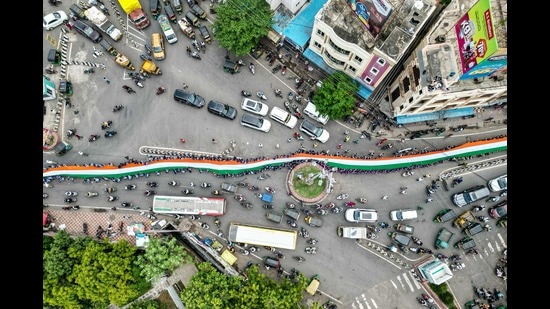 TOPSHOT - An aerial view shows school students carrying a large Indian national flag on a road during the 'Har Ghar Tiranga' campaign on the eve of the country's Independence Day celebrations in Vijayawada on August 14, 2024. (Photo by Idrees MOHAMMED / AFP) (AFP)