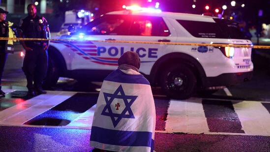 A man, with an Israeli flag with a cross in the center, kneels next to emergency personnel working at the site where, according to the U.S. Homeland Security Secretary, two Israeli embassy staff were shot dead near the Capital Jewish Museum in Washington, D.C., U.S. May 21, 2025.  REUTERS/Jonathan Ernst    TPX IMAGES OF THE DAY