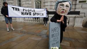 A demonstrator wears a mask depicting Britain's Prime Minister and leader of the Conservative Party Theresa May, poses with a mock gravestone bearing the words A demonstrator wears a mask depicting Britain's Prime Minister and leader of the Conservative Party Theresa May, poses with a mock gravestone bearing the words