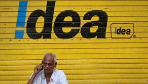 A man speaks on his mobile phone as he sits in front of a shop displaying the Idea Cellular Ltd's logo on its shutter in Mumbai on April 28.(Reuters File) A man speaks on his mobile phone as he sits in front of a shop displaying the Idea Cellular Ltd's logo on its shutter in Mumbai on April 28.(Reuters File)