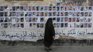 Bahraini woman walks past images of political prisoners plastered on a wall in Sanabis, Bahrain.(AP File Photo)