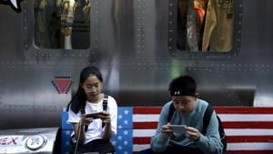 Shoppers sit on a bench with a decorated with US flag browsing their smartphones outside a fashion boutique selling US brand clothing at the capital city's popular shopping mall in Beijing.(AP File Photo) Shoppers sit on a bench with a decorated with US flag browsing their smartphones outside a fashion boutique selling US brand clothing at the capital city's popular shopping mall in Beijing.(AP File Photo)
