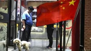 A man walks his dog as he leaves a restaurant flying the Chinese national flag in Beijing, China.(AP Photo) A man walks his dog as he leaves a restaurant flying the Chinese national flag in Beijing, China.(AP Photo)