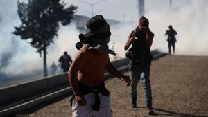 A migrant with his face covered runs from tear gas released by U.S border patrol near the fence between Mexico and the United States in Tijuana, Mexico.(REUTERS) A migrant with his face covered runs from tear gas released by U.S border patrol near the fence between Mexico and the United States in Tijuana, Mexico.(REUTERS)