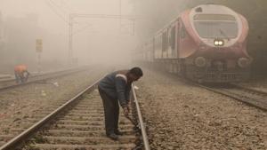 Indian railways employees carry on repair works along a railway track as a train passes by amidst dense fog near a railway station in Amritsar.(AFP)