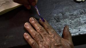 An election officer puts indelible ink mark on the index finger of an elderly voter at a polling centre.(AP)