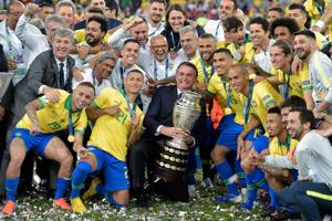Brazilian President Jair Bolsonaro holds the Copa America trophy as members of the national team celebrates after winning the title at Maracana Stadium in Rio de Janeiro.(AFP) Brazilian President Jair Bolsonaro holds the Copa America trophy as members of the national team celebrates after winning the title at Maracana Stadium in Rio de Janeiro.(AFP)