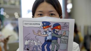 A woman holds up a cartoon depicting police feigning ignorance of thugs attacking protesters as she joins protesters during a second day of sit-in protest at the airport in Hong Kong.(AP) A woman holds up a cartoon depicting police feigning ignorance of thugs attacking protesters as she joins protesters during a second day of sit-in protest at the airport in Hong Kong.(AP)