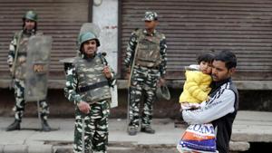 A man carrying a child walks past security forces in a riot affected area following clashes between people demonstrating for and against a new citizenship law in New Delhi.(REUTERS) A man carrying a child walks past security forces in a riot affected area following clashes between people demonstrating for and against a new citizenship law in New Delhi.(REUTERS)