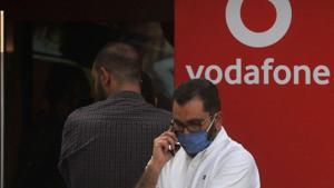 A man wearing a protective face mask talks on his mobile and waits with others outside a branch of Vodafone.(REUTERS) A man wearing a protective face mask talks on his mobile and waits with others outside a branch of Vodafone.(REUTERS)