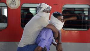A migrant worker carries his brother on his back as they wait to board a special train to return to Agra in Uttar Pradesh state, during the Covid-19 lockdown, in Ahmedabad on Saturday.(AP Photo) A migrant worker carries his brother on his back as they wait to board a special train to return to Agra in Uttar Pradesh state, during the Covid-19 lockdown, in Ahmedabad on Saturday.(AP Photo)