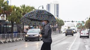 A pedestrian, carrying an umbrella and wearing a mask, crosses Ocean Boulevard in Myrtle Beach, as Tropical Storm Bertha lashes the South Carolina coast on Wednesday.(AP Photo) A pedestrian, carrying an umbrella and wearing a mask, crosses Ocean Boulevard in Myrtle Beach, as Tropical Storm Bertha lashes the South Carolina coast on Wednesday.(AP Photo)