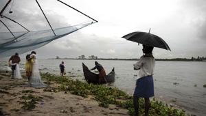 File photo: A man holding an umbrella watches fishermen at work on the Arabian sea coast during monsoon rains in Kochi, Kerala.(AP) File photo: A man holding an umbrella watches fishermen at work on the Arabian sea coast during monsoon rains in Kochi, Kerala.(AP)