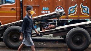 A man wearing a protective face mask walks past a labourer resting on a handcart in a closed wholesale market in West Bengal.(REUTERS) A man wearing a protective face mask walks past a labourer resting on a handcart in a closed wholesale market in West Bengal.(REUTERS)