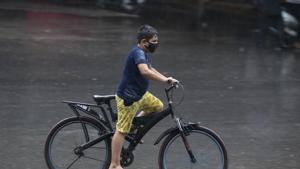 An Indian boy wearing a face mask as a precaution against the coronavirus pedals a bicycle in the rain in Hyderabad, India.(AP) An Indian boy wearing a face mask as a precaution against the coronavirus pedals a bicycle in the rain in Hyderabad, India.(AP)