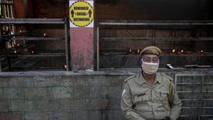 A security person sits wearing a mask outside a temple in Guwahati.(AP) A security person sits wearing a mask outside a temple in Guwahati.(AP)