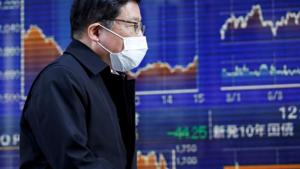 A passerby wearing a protective face mask walks past an electronic board showing the graphs of the recent movements of Japan's Nikkei share average outside a brokerage in Tokyo, Japan.(Reuters) A passerby wearing a protective face mask walks past an electronic board showing the graphs of the recent movements of Japan's Nikkei share average outside a brokerage in Tokyo, Japan.(Reuters)