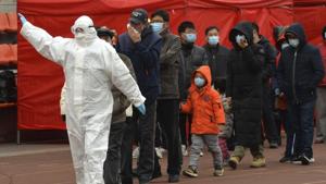 A worker wearing a protective suit gestures to a line of people at a Covid-19 testing site in Tianjin, China, on Saturday.(AP) A worker wearing a protective suit gestures to a line of people at a Covid-19 testing site in Tianjin, China, on Saturday.(AP)