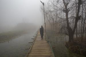 A Kashmiri man shields his face from cold as he walks over a foot bridge through dense fog on a cold morning on the outskirts of Srinagar on Thursday.(AP) A Kashmiri man shields his face from cold as he walks over a foot bridge through dense fog on a cold morning on the outskirts of Srinagar on Thursday.(AP)