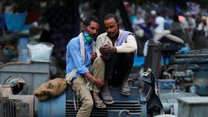 Men wearing protective face masks on their chins, amid the coronavirus disease outbreak, watch a video on a mobile phone as they sit at a second-hand motor parts market in the old quarters of Delhi.(REUTERS) Men wearing protective face masks on their chins, amid the coronavirus disease outbreak, watch a video on a mobile phone as they sit at a second-hand motor parts market in the old quarters of Delhi.(REUTERS)