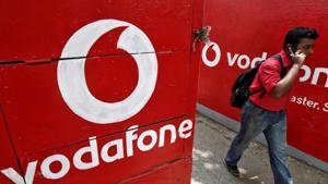 A man speaks on his mobile phone as he walks past logos of Vodafone painted on a roadside wall in Kolkata.(REUTERS) A man speaks on his mobile phone as he walks past logos of Vodafone painted on a roadside wall in Kolkata.(REUTERS)