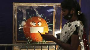 A woman wears a face mask on her chin and walks past a cake depicting the coronavirus on display at the annual cake show organized as part of new year celebrations in Bengaluru, India.(AP) A woman wears a face mask on her chin and walks past a cake depicting the coronavirus on display at the annual cake show organized as part of new year celebrations in Bengaluru, India.(AP)