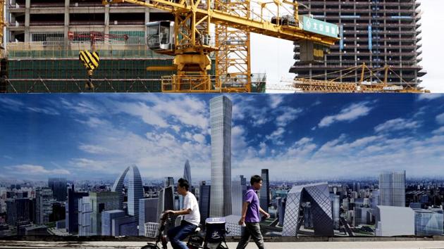 A man on a motorbike and a pedestrian pass by a construction site wall depicting the skyline of the Chinese capital in Beijing. (AP File Photo) A man on a motorbike and a pedestrian pass by a construction site wall depicting the skyline of the Chinese capital in Beijing. (AP File Photo)