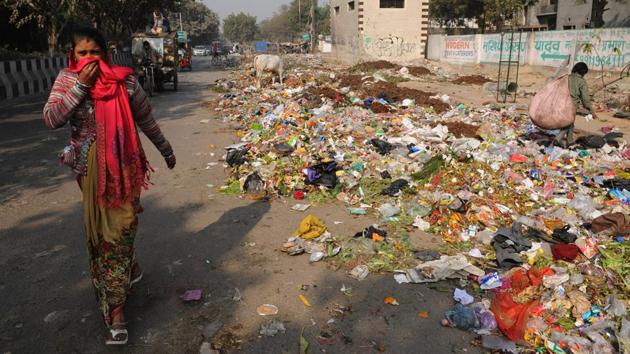 A woman covers her nose while walking past a garbage dump at Nithari village in Sector 29. Residents are being inconvenienced because of the growing mounds of waste on roads and residential areas. (Burhaan Kinu/HT PHOTO)