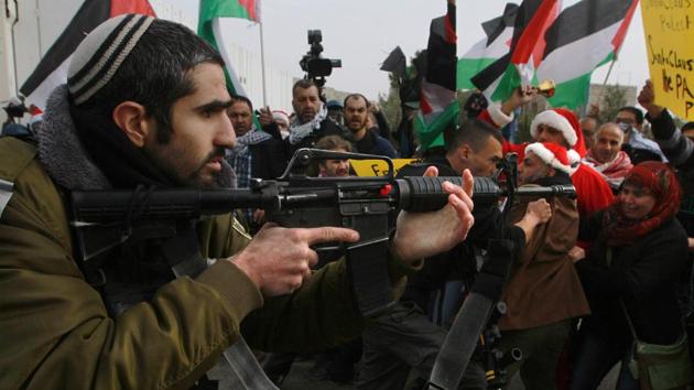 Israeli soldier aims his weapon at Palestinian protestors, some dressed up as Santa Claus, during a demonstration next to a gate of a section of Israel's separation wall in the biblical town of Bethlehem, in the occupied West Bank, on Friday.(AFP) Israeli soldier aims his weapon at Palestinian protestors, some dressed up as Santa Claus, during a demonstration next to a gate of a section of Israel's separation wall in the biblical town of Bethlehem, in the occupied West Bank, on Friday.(AFP)