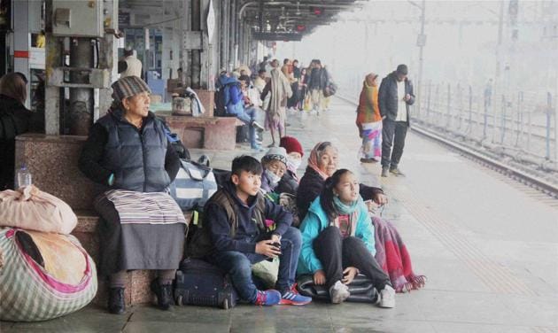 Stranded passengers wrap themselves in warm clothes as they wait for their trains, delayed due to fog in Allahabad. (PTI)