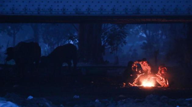 WINTER BLUES: As night draws to an end and morning light begins to spread around, people gather around a bonfire near Yamuna bank for warmth. (AMAL KS/HT PHOTO) 