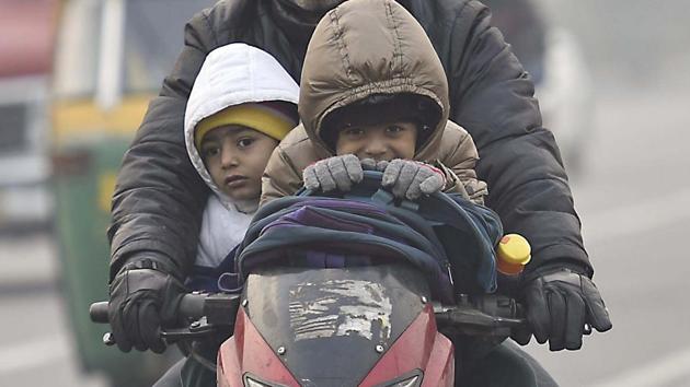 Two boys wearing jackets and holding a protective layer as their father rides them to school on a cold winter morning in New Delhi. (Raj K Raj/HT Photo)