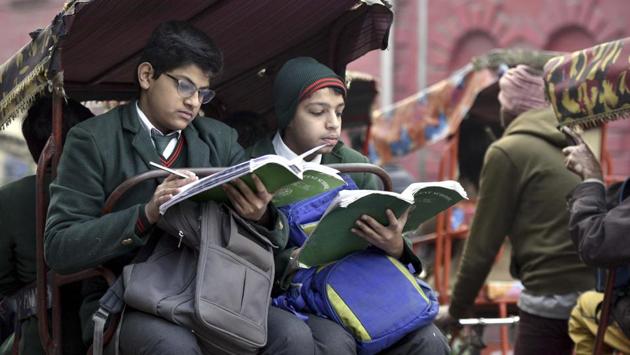 Schoolchildren engrossed in studies as they ride on the back of a cycle-rickshaw to school. (Arun Sharma/HT PHOTO)