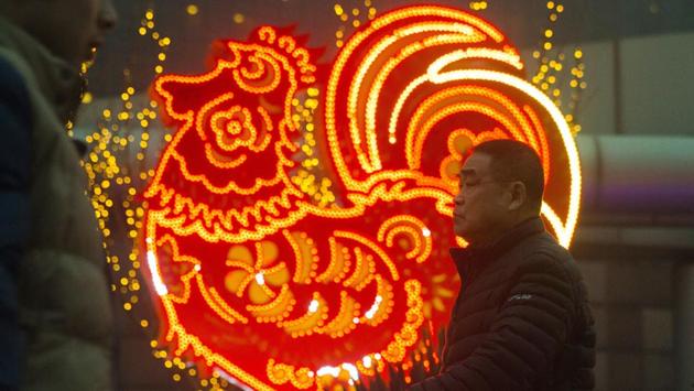 Chinese men walk past neon decorations marking the Year of the Rooster in Beijing on Monday. (Ng Han Guan) / AP)