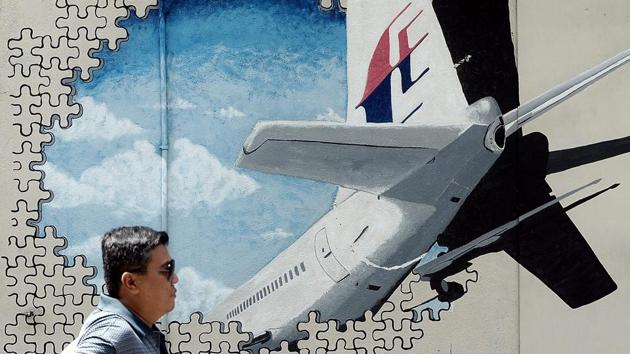This file picture taken on March 8, 2016 shows a man walking in front of a mural of missing Malaysia Airlines MH370 plane in a back-alley in Shah Alam, Malaysia. The deep ocean hunt for MH370 has been suspended after nearly three years without result, the Australian, Malaysian and Chinese governments have said. (AFP)