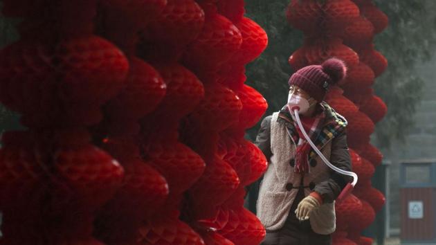 An elderly woman wearing a home-made mask walks past lanterns hung ahead of the Lunar New Year at a park in Beijing on Tuesday. (WANG Zhao / AFP)