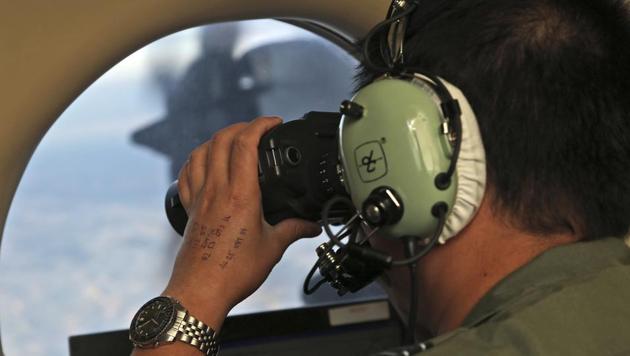 In this March 22, 2014, file photo, Flight Officer Jack Chen uses binoculars at an observers window on a Royal Australian Air Force P-3 Orion during the search for Flight MH370. (AP)