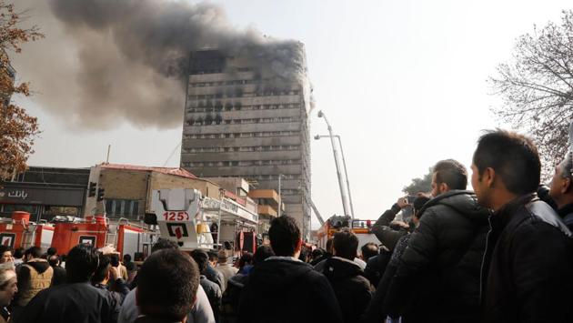 People watch as firefighters try to douse the fire . (AFP) People watch as firefighters try to douse the fire . (AFP)