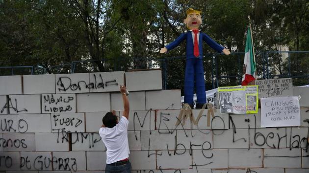 A demonstrator writes on symbolic wall as is seen a pinata representing the US President Donald Trump during a protest outside the US embassy, in Mexico City, Mexico on January 20, 2017.(REUTERS)