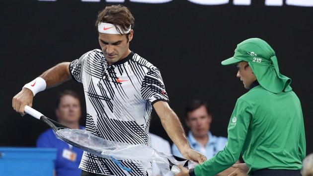 Roger Federer unwraps a new racket during the Australian Open final on Sunday. (AP)