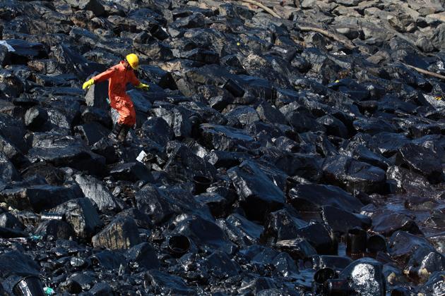 An emergency worker walks amidst oil deposits as he cleans oil from the shoreline of Ennore port in Chennai. (REUTERS) An emergency worker walks amidst oil deposits as he cleans oil from the shoreline of Ennore port in Chennai. (REUTERS)
