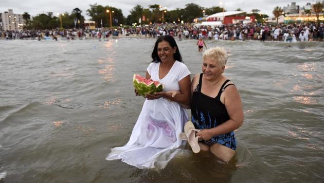 Two women enter the sea with an offering for the African sea goddess Yemanja, during a ceremony honoring the deity in Montevideo, Uruguay, Thursday, Feb. 2, 2017. (Matilde Campodonico / AP)